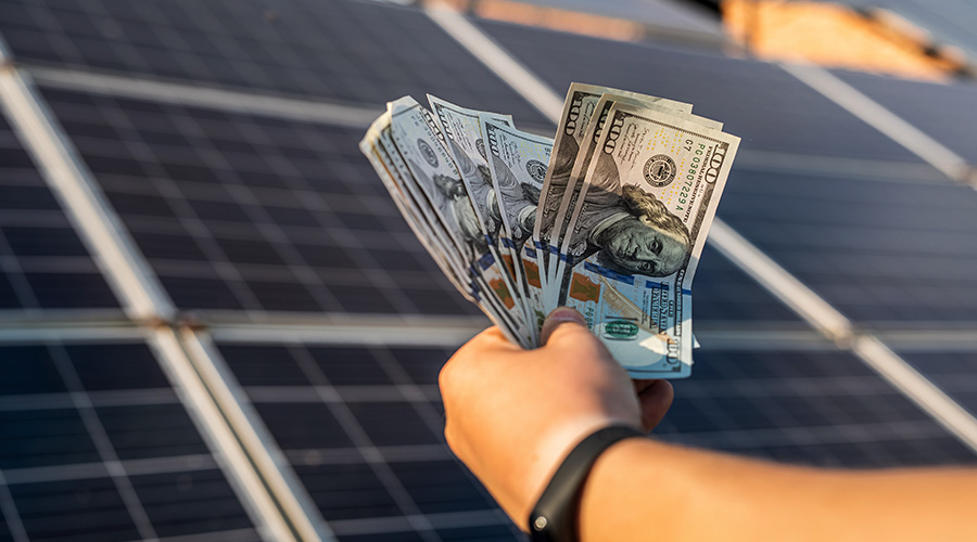 hand holding dollar bills in front of solar panels