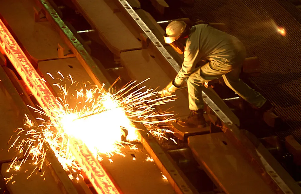 Steel worker cuts through billet as sparks fly in mill